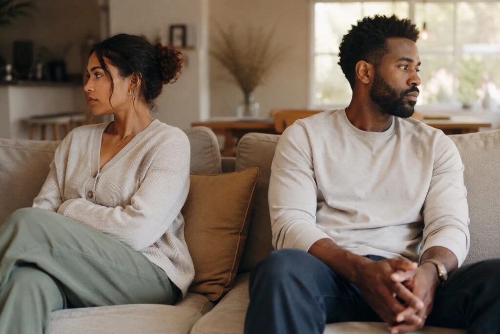 Couple stuck in a recurring fight, sitting apart and disconnected on the couch